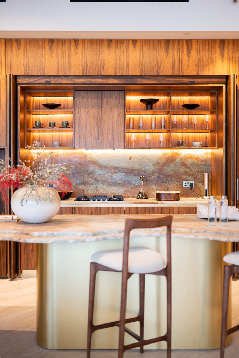 Walnut kitchen with lit open shelving, stone splashback and brass island