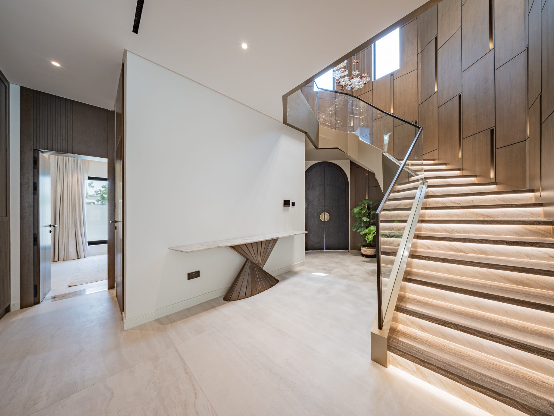 Entrance hall with arched front door and lit travertine staircase