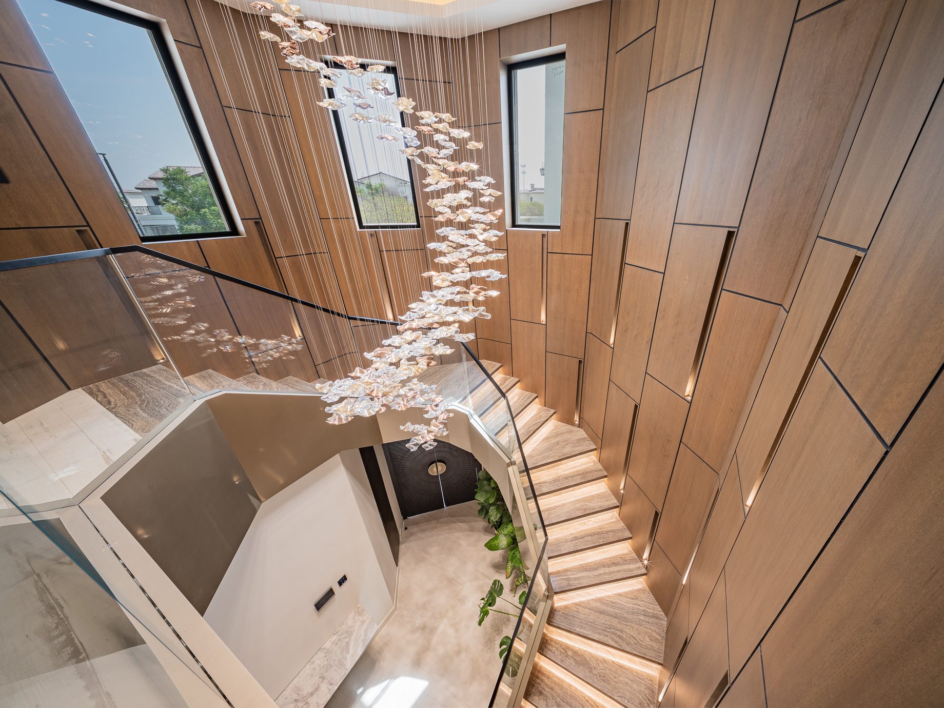 Glass and travertine staircase beneath a suspended crystal chandelier